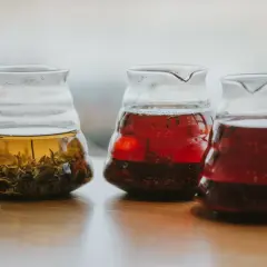 Trzy szklane dzbanki z zaparzonymi herbatami: jasnożółtą z liśćmi, czerwoną i ciemnoczerwoną, być może lapsang souchong.