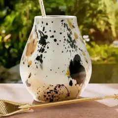 Elegancki matero, czyli jak się nazywa kubek do yerba mate, z ozdobnym wzorem i złotą bombillą na tle zieleni.