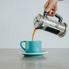 Nalewanie aromatycznej herbaty z french pressa do turkusowej filiżanki.