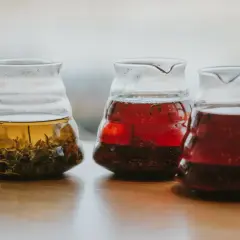 Trzy szklane dzbanki z naparami: jasny, czerwony i ciemnoczerwony. W pierwszym widać liście, jakby z Ilex vomitoria.
