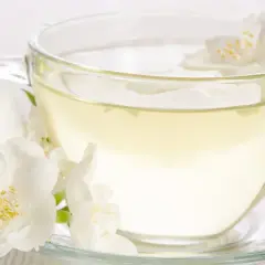 Aromatyczna biała herbata z jaśminem w szklanej filiżance. Czy biała herbata pobudza? Delikatny napar i kwiaty sugerują relaks.
