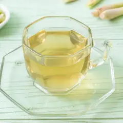 Aromatyczna herbata z trawy cytrynowej w szklanej filiżance, obok świeże łodygi i plasterki.