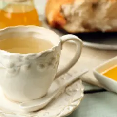 Ciepła herbatka imbirowa w ozdobnej filiżance, obok miód i kawałek chleba. Idealny poranek.