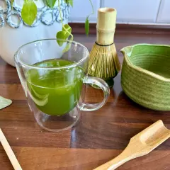 Zielona matcha w szklance, obok bambusowa miotełka i łopatka. Poznaj, jak smakuje matcha!