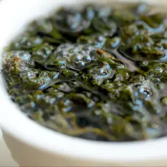 Zielone liście herbaty oolong w wodzie, uwalniające swoje cenne właściwości. Bąbelki unoszą się na powierzchni.