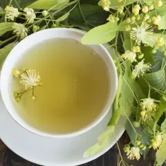 Kubek aromatycznej herbaty z lipy, idealnej na kaszel, otoczony świeżymi kwiatami i liśćmi lipy.
