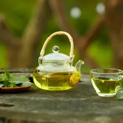 Szklany dzbanuszek i filiżanka z aromatyczną, najlepszą herbatą cejlońską, ozdobione świeżymi listkami na drewnianym blacie.