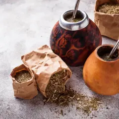 Dwa tykwy z yerba mate i bombillami, obok papierowe torebki z suszem. Czy yerbę można słodzić? To zależy od preferencji!