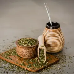 Drewniana miseczka i łopatka pełne suszonej yerba mate, obok ceramiczny naczynie z bombillą. Napar z yerba mate wspiera wątrobę.
