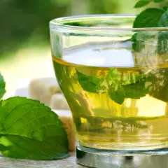 Herbatka z mięty, idealna na zgagę w ciąży. Świeże liście mięty i kostki cukru obok szklanki naparu.