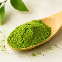 Łyżka z zielonym proszkiem matcha, który pobudza. Obok liście.