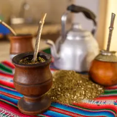 Tradycyjny rytuał z yaguar yerba mate: drewniane naczynia, bombille i czajnik na kolorowym obrusie.