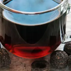 Szklanka z aromatycznym, czerwonym herbatą, otoczona sprasowanymi liśćmi, gotowa do zaparzenia.