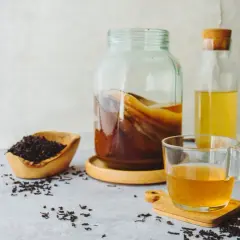 Słoik z kombuchą, miseczka z liśćmi herbaty i szklanka gotowego napoju. Oto jak zrobic kombuche w domu.