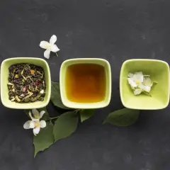 Trzy zielone miseczki na ciemnym tle: jedna z suszoną herbatą, druga z bursztynowym naparem, trzecia z białymi kwiatami jaśminu. Poczuj aromat koreańskiej herbaty.