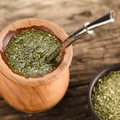 Drewniane naczynie z yerba mate na uspokojenie, obok miseczka z suszem. Metalowa bombilla zanurzona w naparze.
