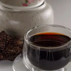 Ciemna, aromatyczna czerwona herbata w szklance, obok sprasowane liście. Idealna na pobudzenie rano lub relaks wieczorem.
