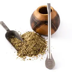 Naczynie z tykwy, metalowa bombilla i garść suszu do yerba mate. Różne rodzaje yerba mate czekają na zaparzenie.