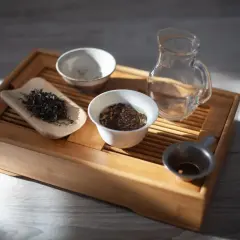 Zestaw do gongfu cha: drewniana taca, liście herbaty, czajniczek, miseczki i sitko.