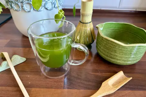 Zielona matcha w szklance, obok bambusowa miotełka i łopatka. Poznaj, jak smakuje matcha!