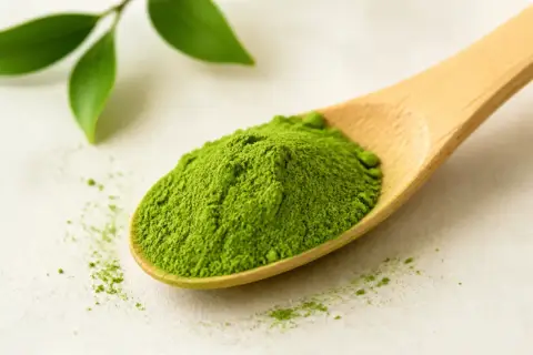 Łyżka z zielonym proszkiem matcha, który pobudza. Obok liście.