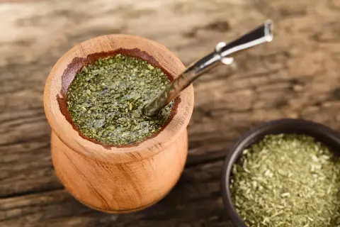 Drewniane naczynie z yerba mate na uspokojenie, obok miseczka z suszem. Metalowa bombilla zanurzona w naparze.