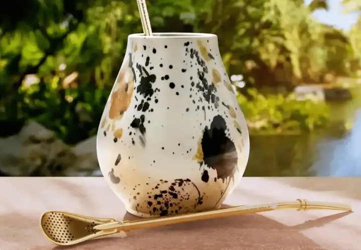 Elegancki matero, czyli jak się nazywa kubek do yerba mate, z ozdobnym wzorem i złotą bombillą na tle zieleni.