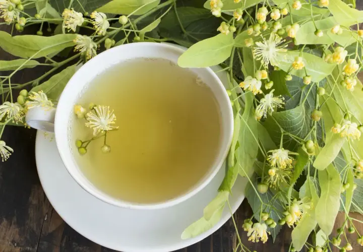 Kubek aromatycznej herbaty z lipy, idealnej na kaszel, otoczony świeżymi kwiatami i liśćmi lipy.