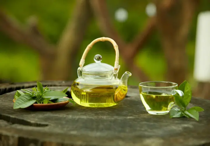 Szklany dzbanuszek i filiżanka z aromatyczną, najlepszą herbatą cejlońską, ozdobione świeżymi listkami na drewnianym blacie.