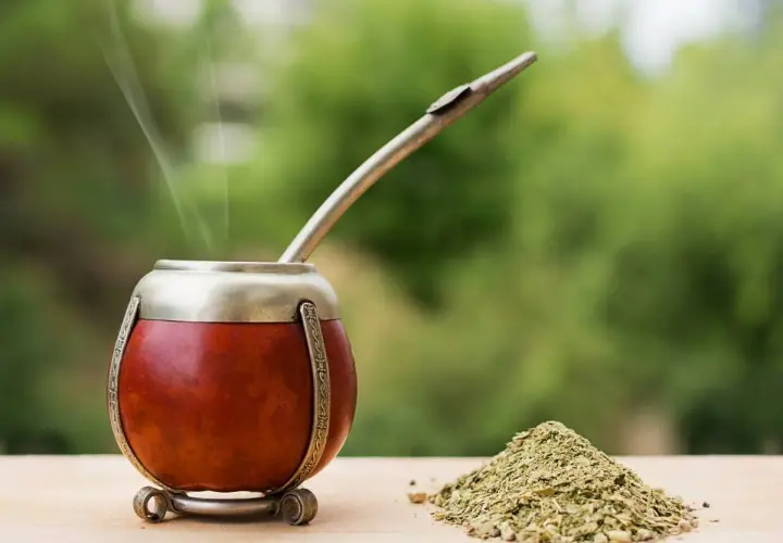 Parząca yerba mate Guarani w tykwie, z metalową bombillą i górką suszu na drewnianym blacie.