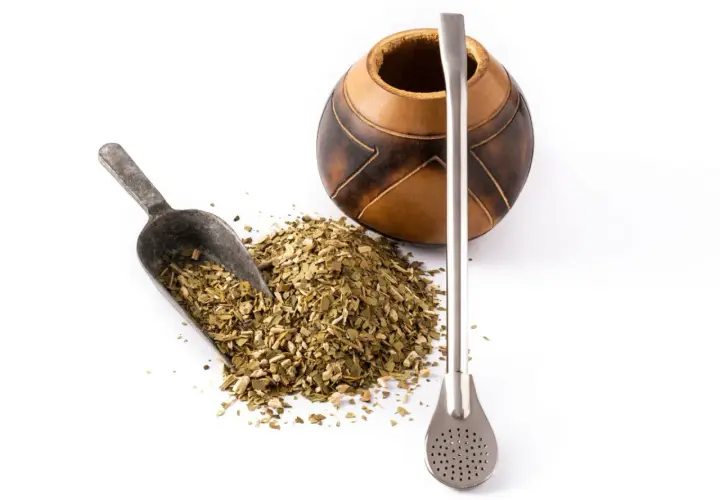 Naczynie z tykwy, metalowa bombilla i garść suszu do yerba mate. Różne rodzaje yerba mate czekają na zaparzenie.
