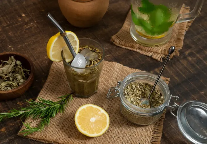 Orzeźwiająca yerba mate cytrynowa z lodem i rozmarynem, obok słoik z suszem i cytryna.