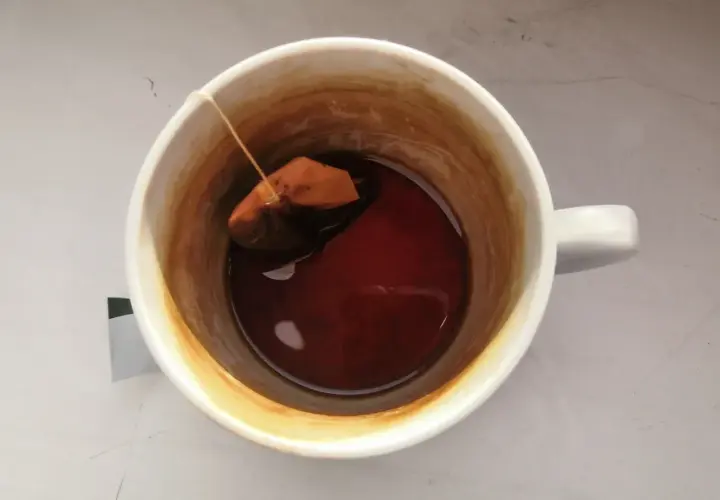 W kubku herbata z widocznym osadem na ściankach. Torebka z herbatą pływa w ciemnym naparze.