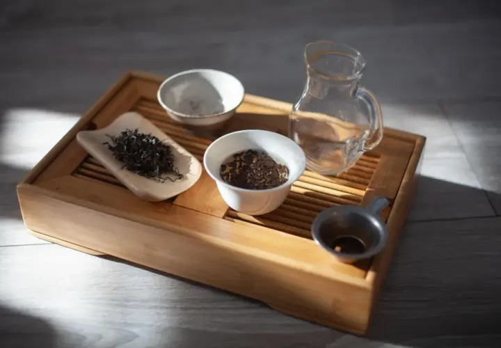 Zestaw do gongfu cha: drewniana taca, liście herbaty, czajniczek, miseczki i sitko.