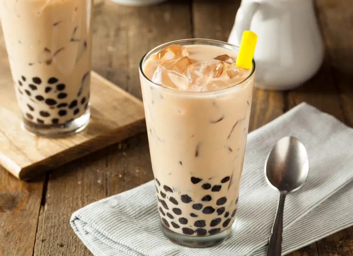 Jak zrobić bubble tea? Dwa szklanki z mlecznym napojem, lodem i czarnymi kuleczkami tapioki, jeden z żółtą słomką.