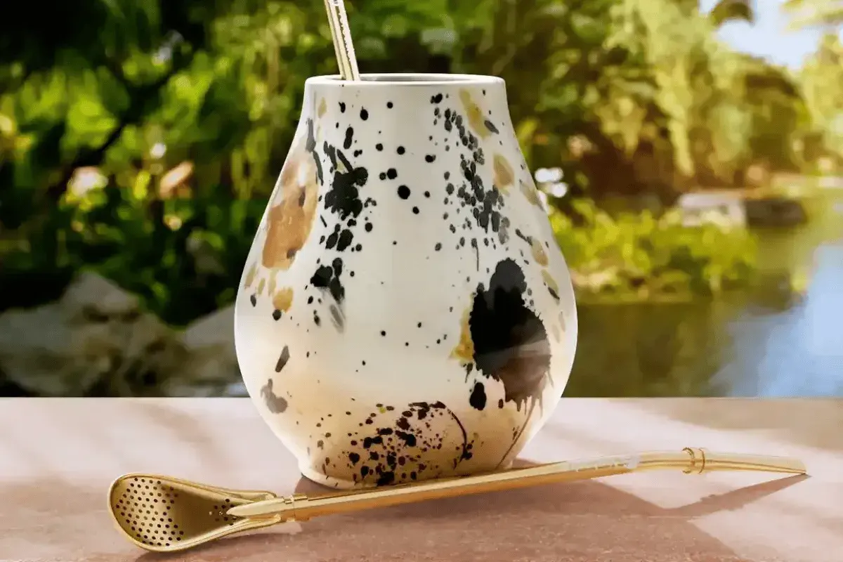Elegancki matero, czyli jak się nazywa kubek do yerba mate, z ozdobnym wzorem i złotą bombillą na tle zieleni.