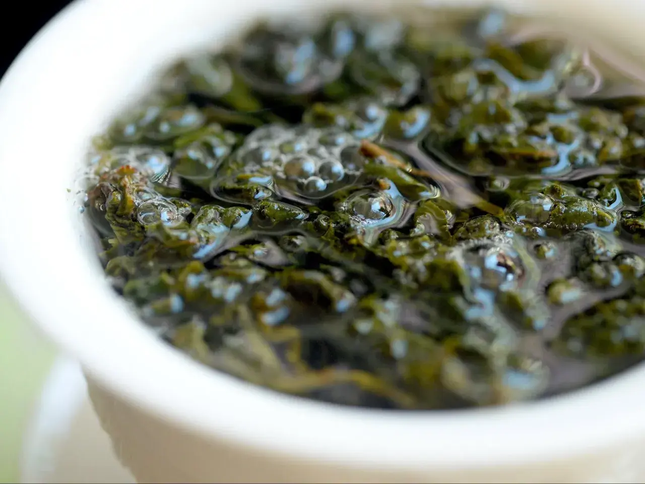 Zielone liście herbaty oolong w wodzie, uwalniające swoje cenne właściwości. Bąbelki unoszą się na powierzchni.