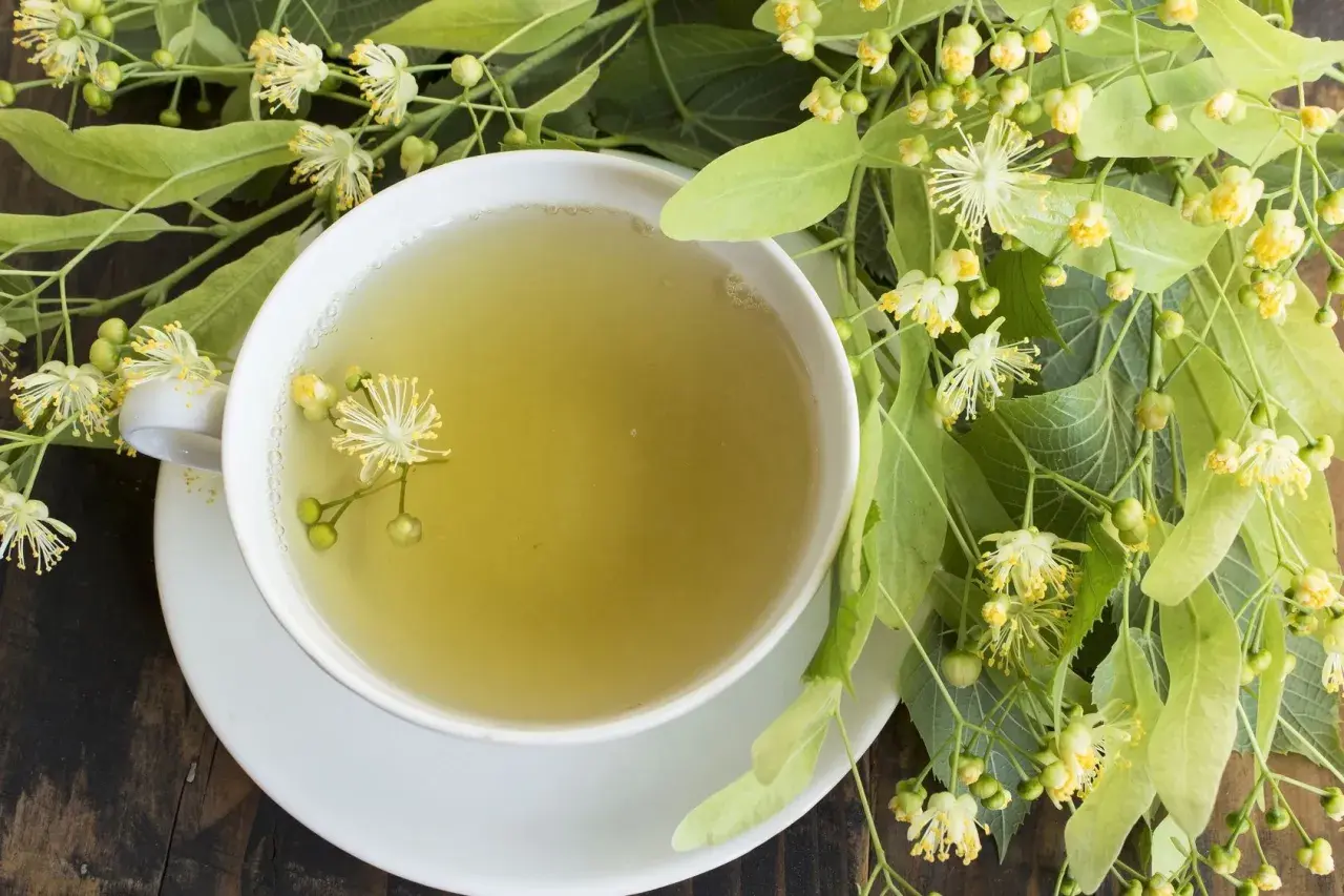 Kubek aromatycznej herbaty z lipy, idealnej na kaszel, otoczony świeżymi kwiatami i liśćmi lipy.