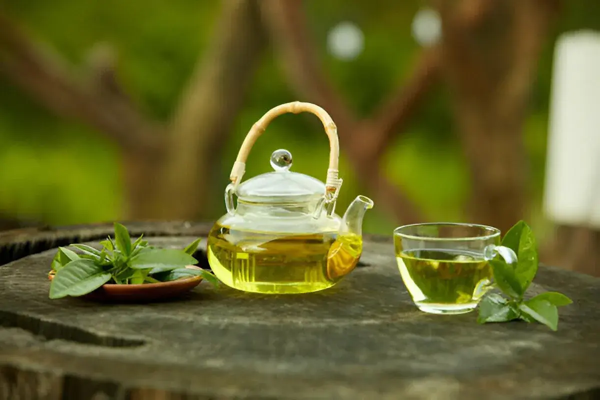 Szklany dzbanuszek i filiżanka z aromatyczną, najlepszą herbatą cejlońską, ozdobione świeżymi listkami na drewnianym blacie.