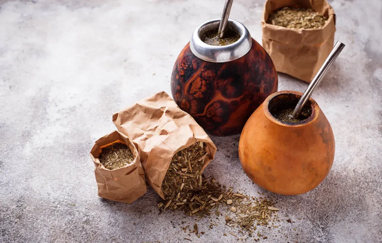Dwa tykwy z yerba mate i bombillami, obok papierowe torebki z suszem. Czy yerbę można słodzić? To zależy od preferencji!