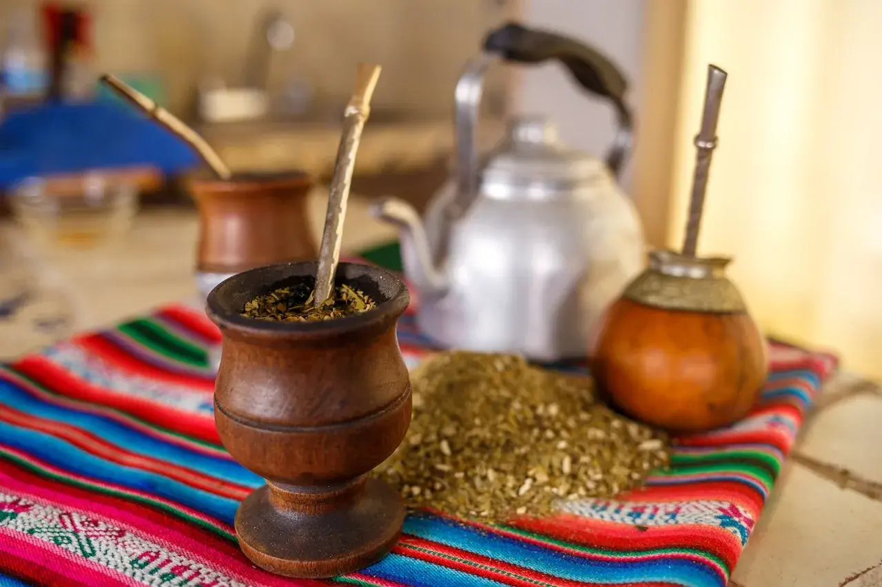 Tradycyjny rytuał z yaguar yerba mate: drewniane naczynia, bombille i czajnik na kolorowym obrusie.