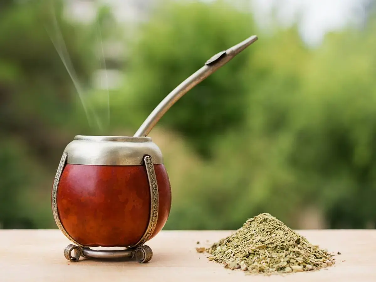 Parząca yerba mate Guarani w tykwie, z metalową bombillą i górką suszu na drewnianym blacie.