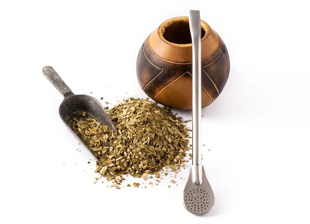 Naczynie z tykwy, metalowa bombilla i garść suszu do yerba mate. Różne rodzaje yerba mate czekają na zaparzenie.