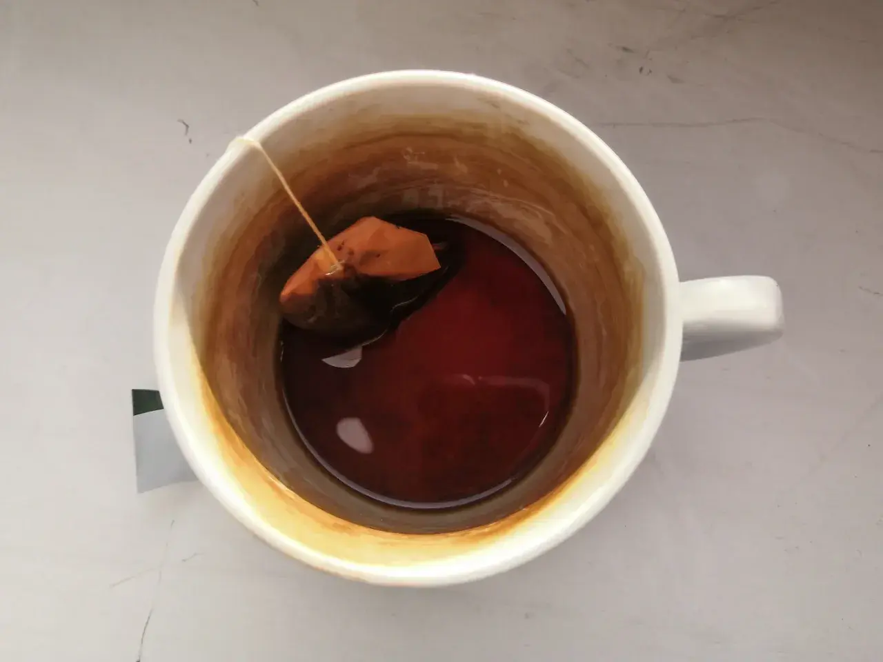 W kubku herbata z widocznym osadem na ściankach. Torebka z herbatą pływa w ciemnym naparze.
