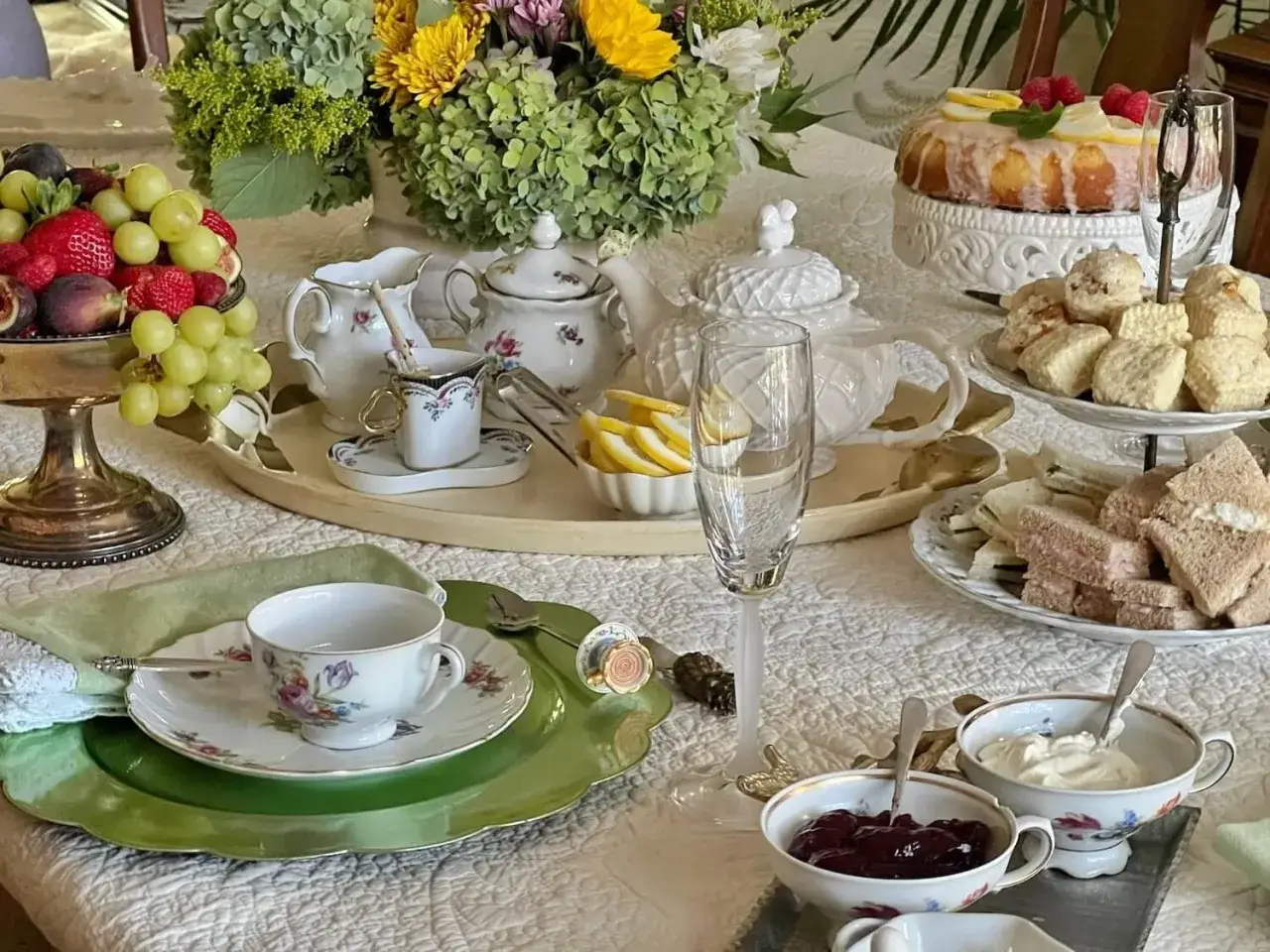 Elegancka herbata po angielsku: babeczki, kanapki, owoce, ciasto cytrynowe i kwiaty tworzą wykwintny stół.