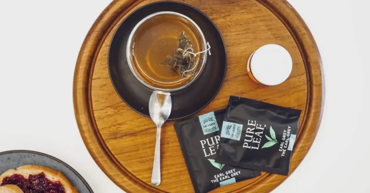 Herbata lapsang souchong w szklance, obok saszetki Earl Grey i tost z dżemem.