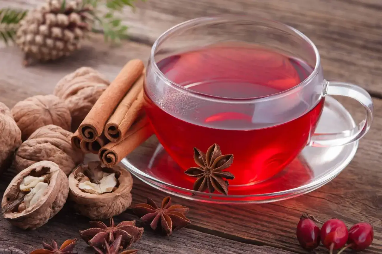 Herbata zimowa przepis z pomarańczą i goździkami. Aromatyczny napój z cynamonem, anyżem i orzechami na drewnianym stole.